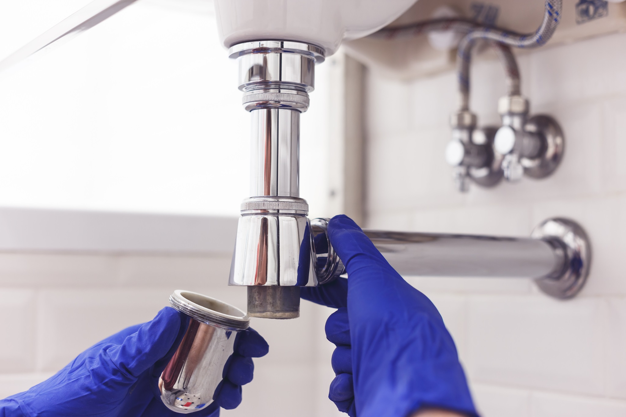 Plumber repairs and maintains chrome siphon under the washbasin. Plumber at work in bathroom, plumbing assemble and install concept.